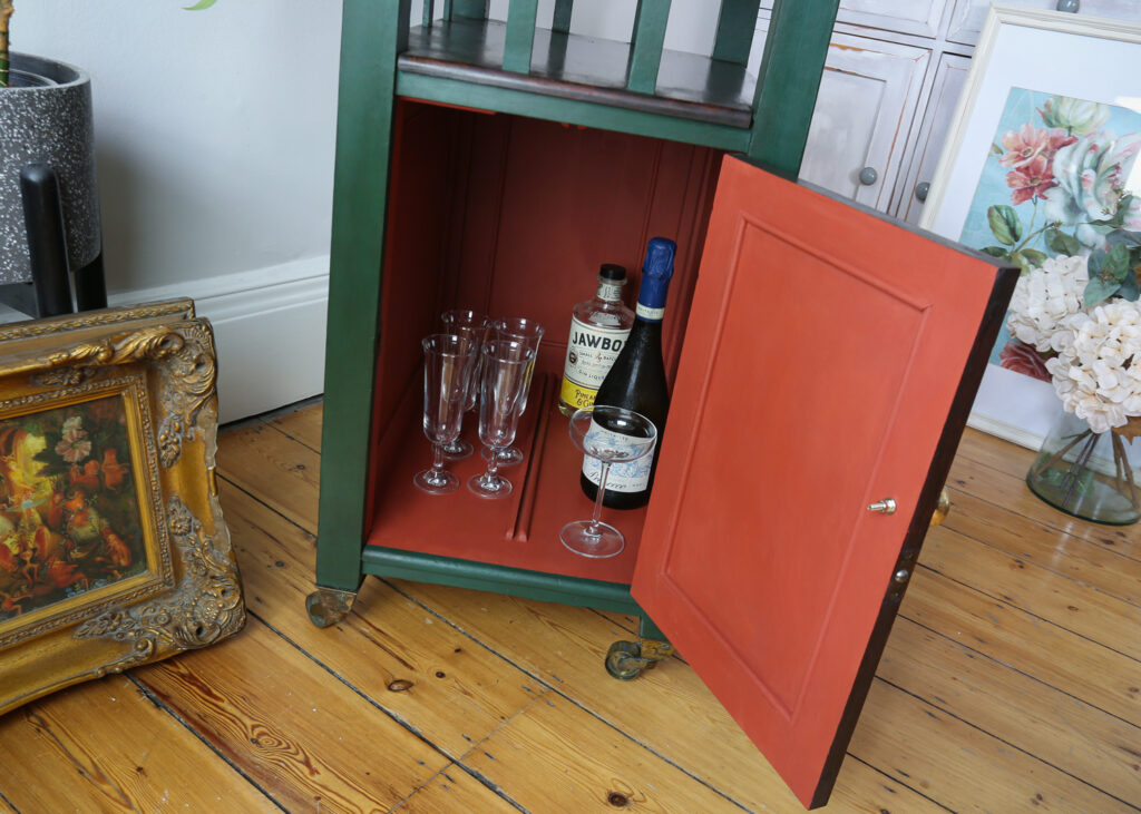 Inside the cupboard of the dark green art deco bar, which is a contrasting but complimentary Paprika Red. Glasses and bottles showcase its use.