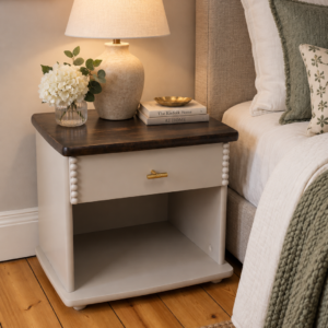 Taupe bedside table by bed with a lamp on the dark wood top