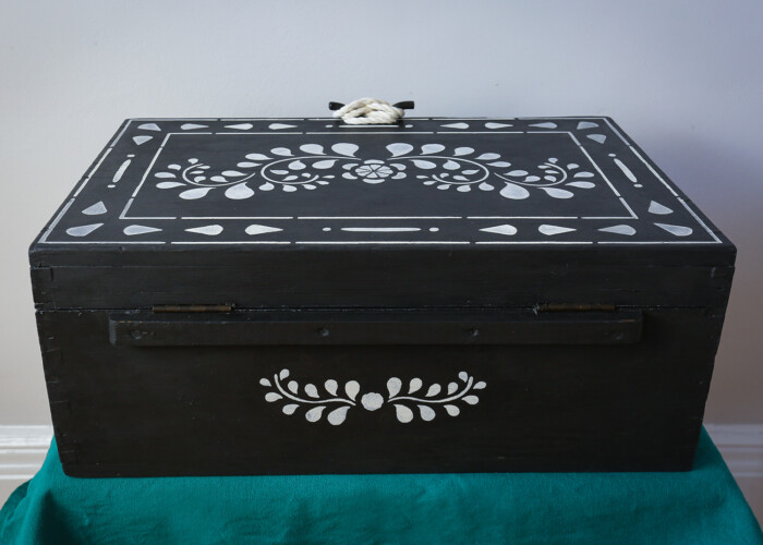 The back of a wooden antique box originally a fisherman's box, hand painted in black, with white floral design on the back. Painted using Annie Sloan paint.