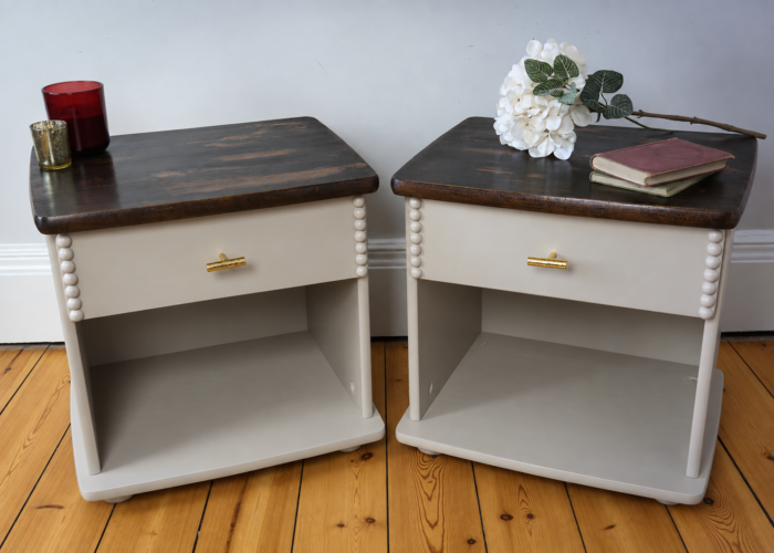 Pair of taupe bedside tables with dark wood tops, with flowers, books and candles